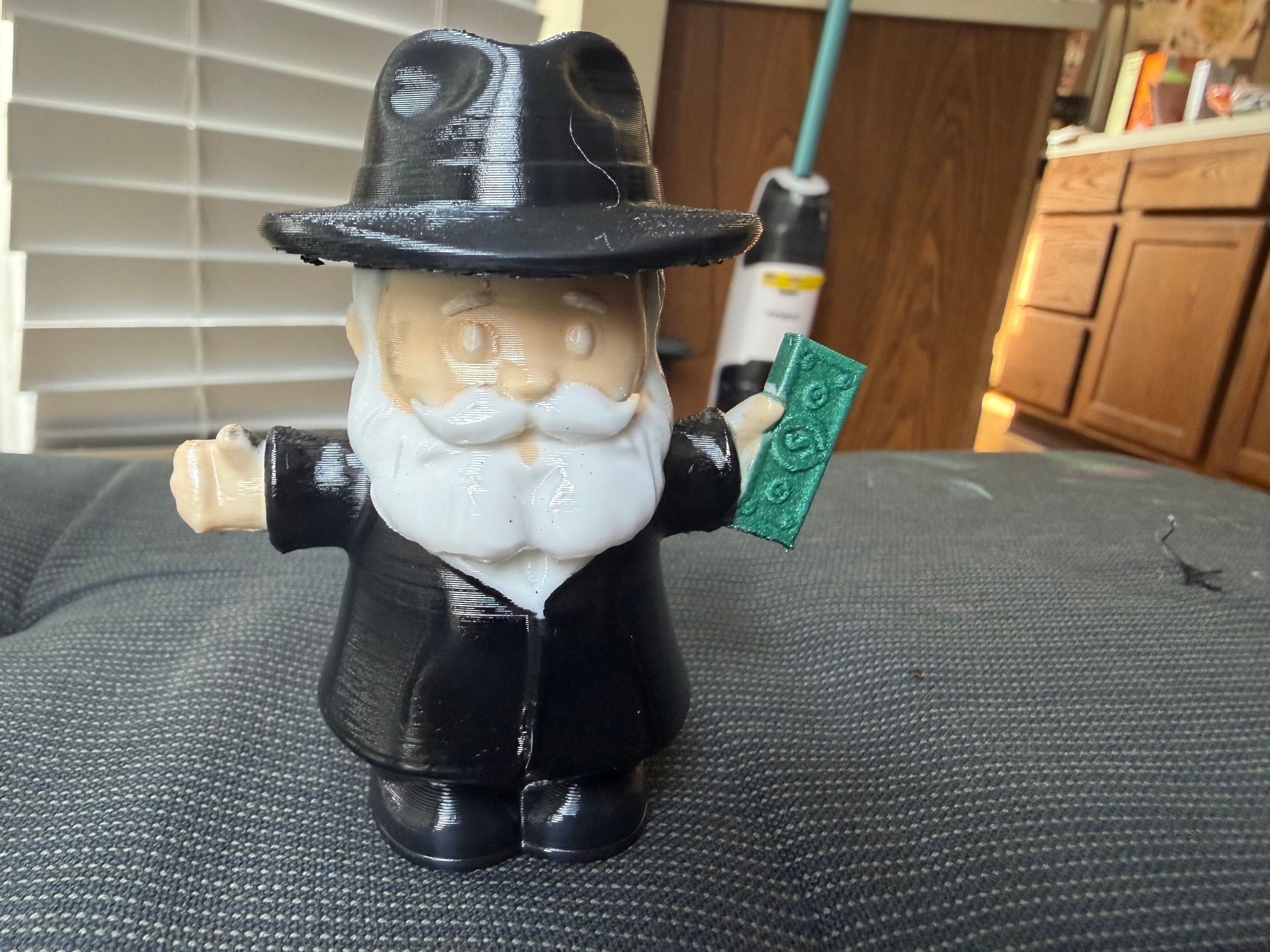 3D printed figurine of an old man in a black hat and coat holding a banknote