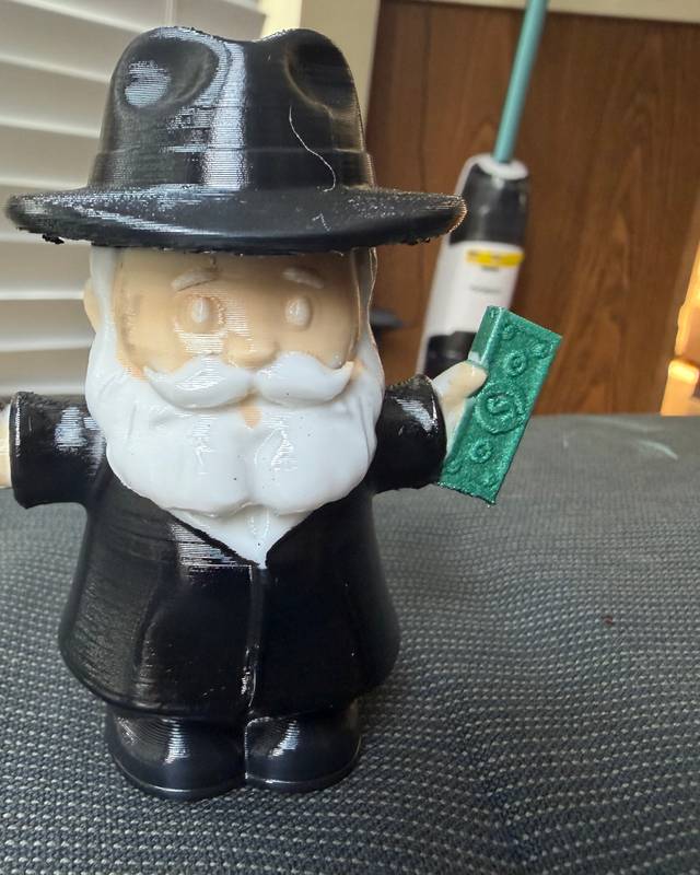 3D printed figurine of an old man in a black hat and coat holding a banknote